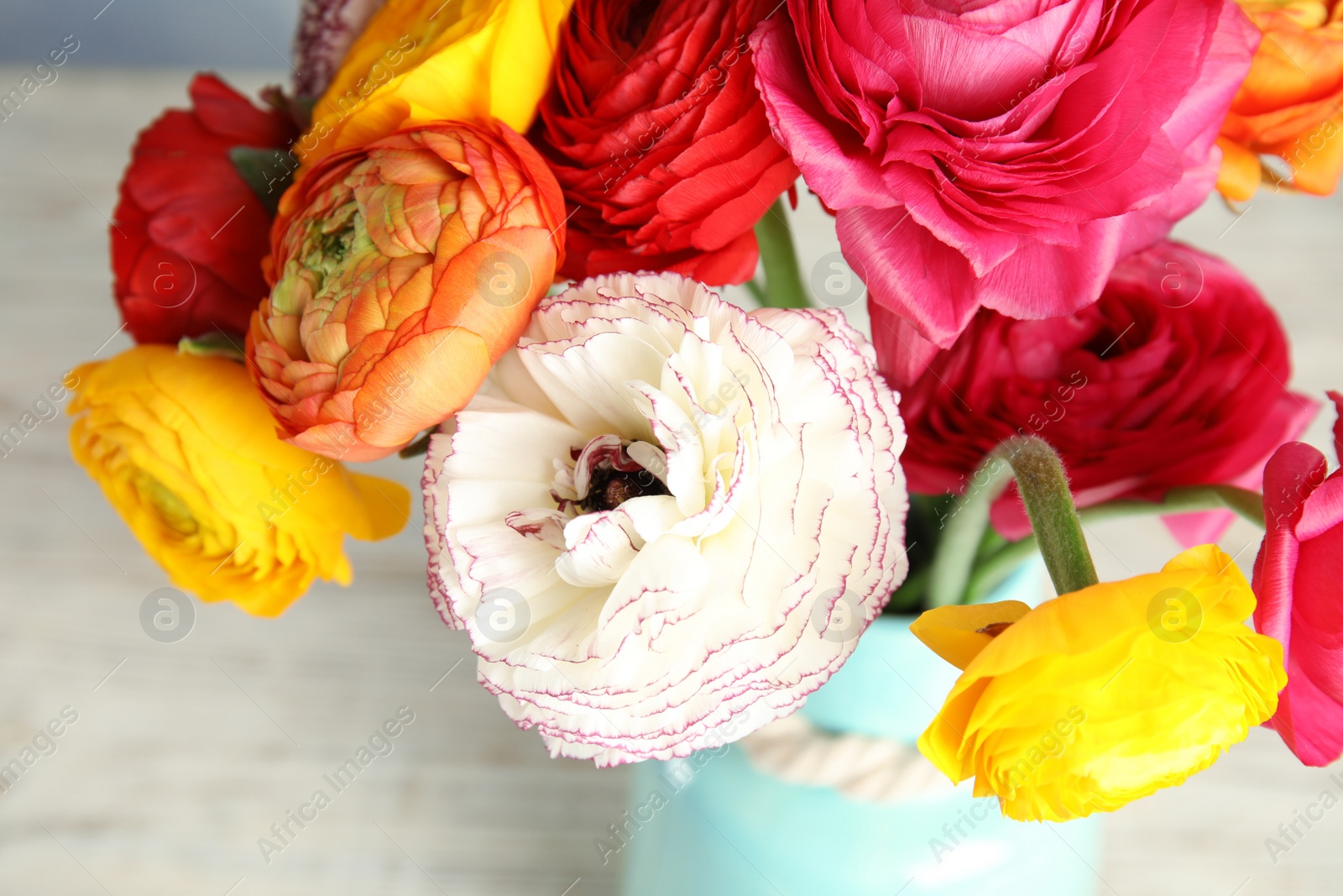 Photo of Bouquet of beautiful bright ranunculus flowers in vase on light table, closeup