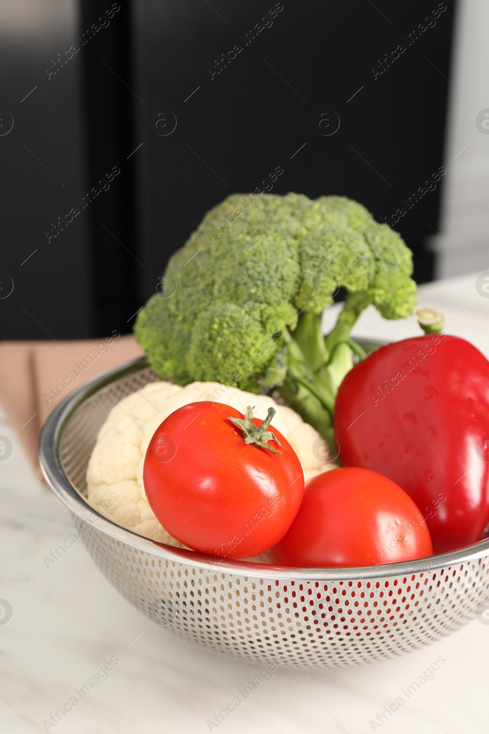 Photo of Colander with different fresh vegetables on white table indoors, closeup