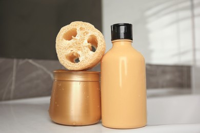 Photo of Natural loofah sponge and cosmetic products on washbasin in bathroom, closeup