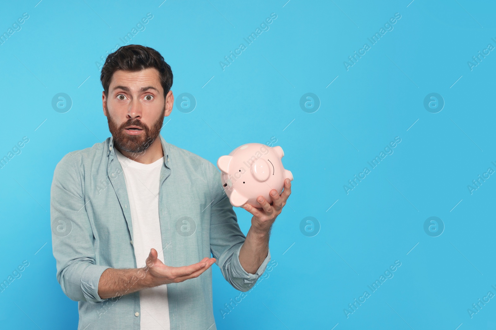 Photo of Man with ceramic piggy bank on light blue background, space for text