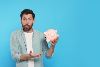 Man with ceramic piggy bank on light blue background, space for text