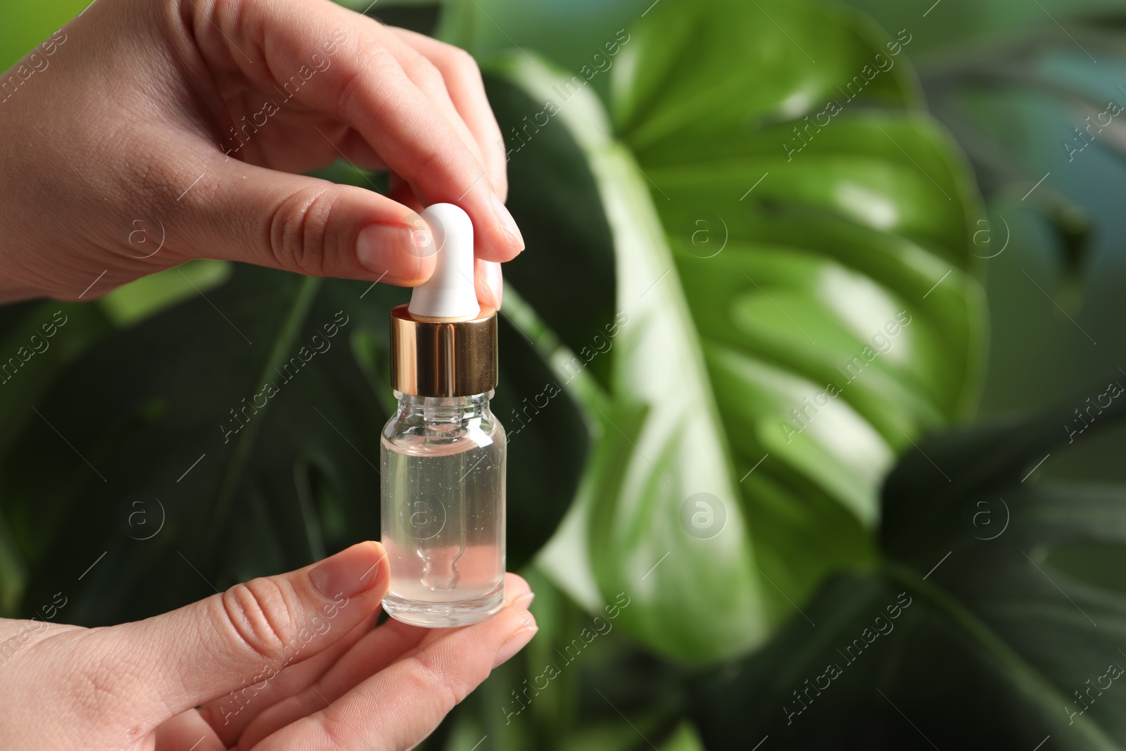 Photo of Woman with bottle of cosmetic serum on blurred background, closeup. Space for text