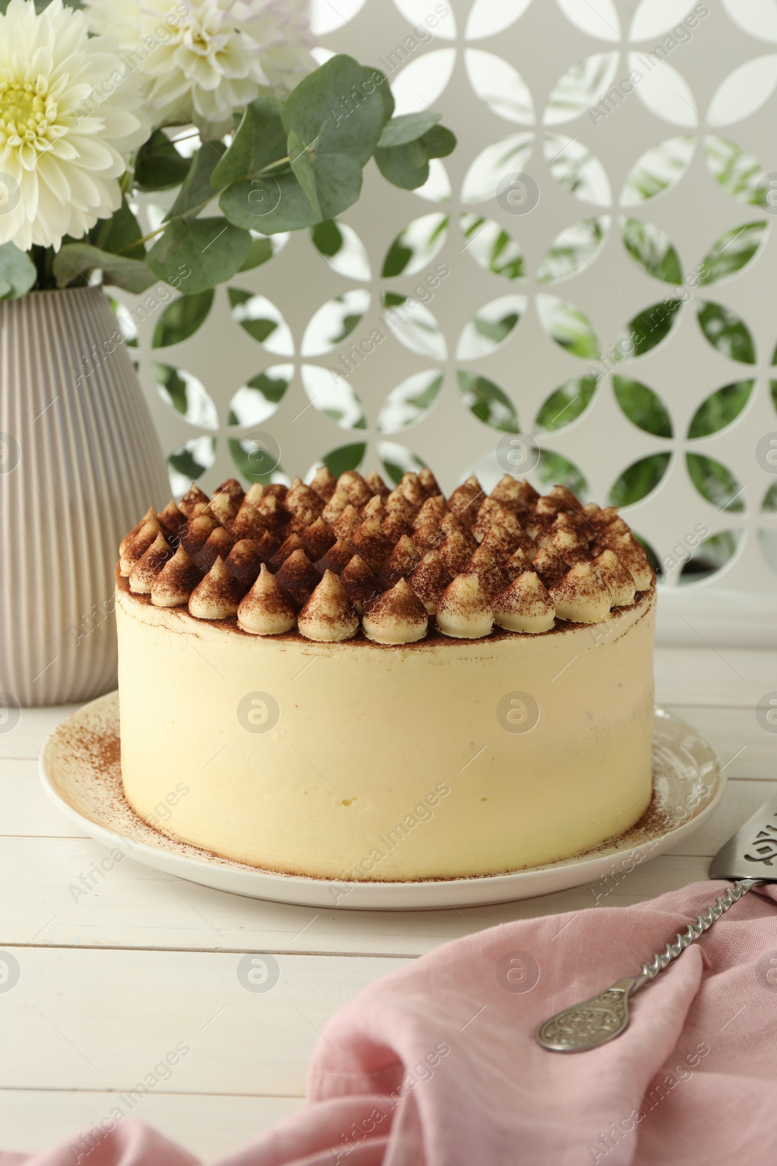 Photo of Delicious tiramisu cake with cocoa powder and server on white wooden table