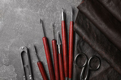 Photo of Leather sample and craftsman tools on grey stone background, flat lay