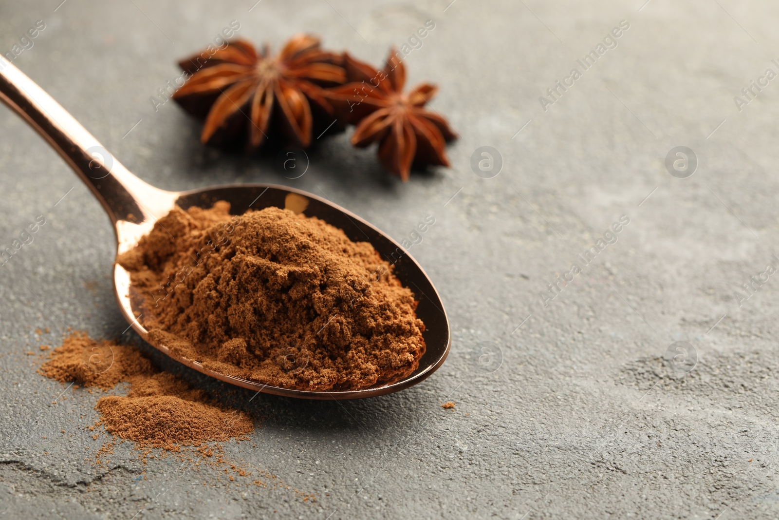Photo of Spoon with cinnamon powder and star anise on grey table, closeup. Space for text
