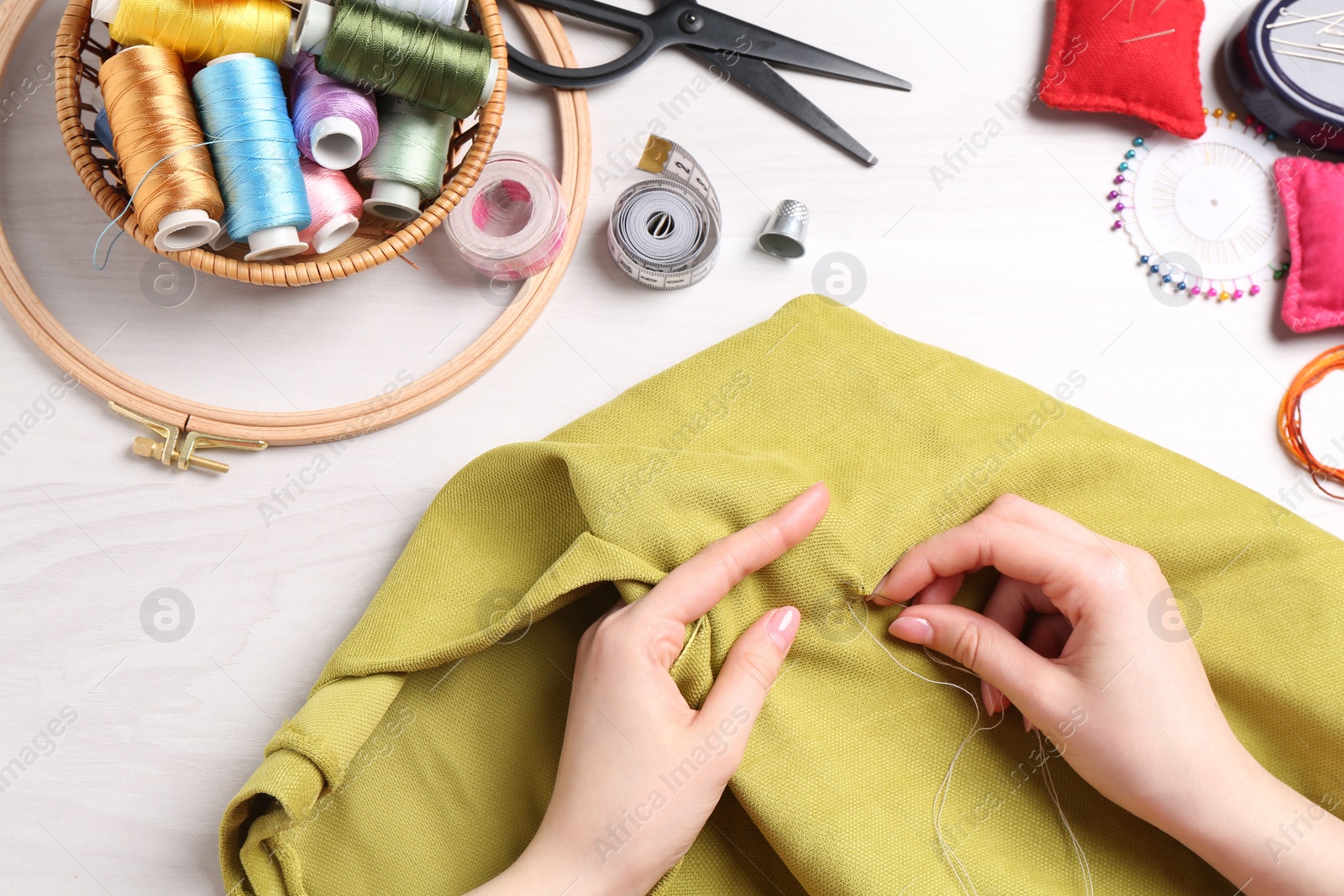 Photo of Woman with sewing thread embroidering on cloth at white wooden table, top view