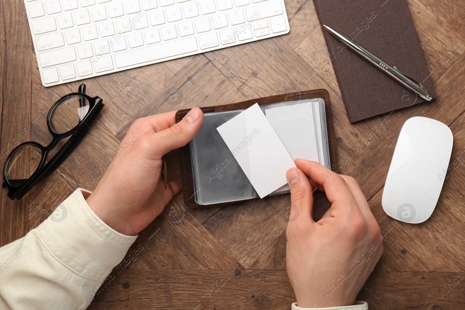 Photo of Man holding leather business card holder with blank cards at wooden table, top view