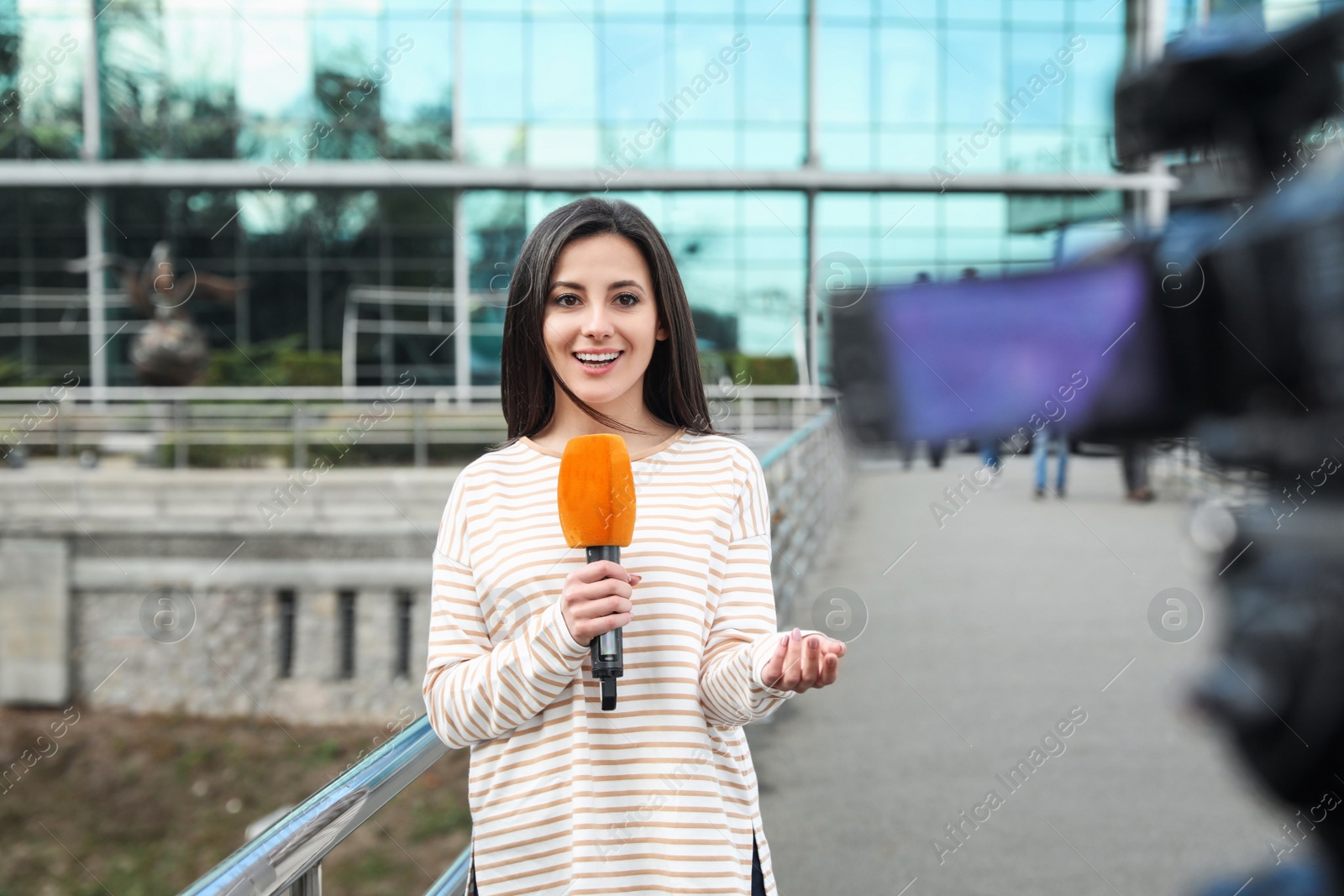 Photo of Young female journalist with microphone working on city street