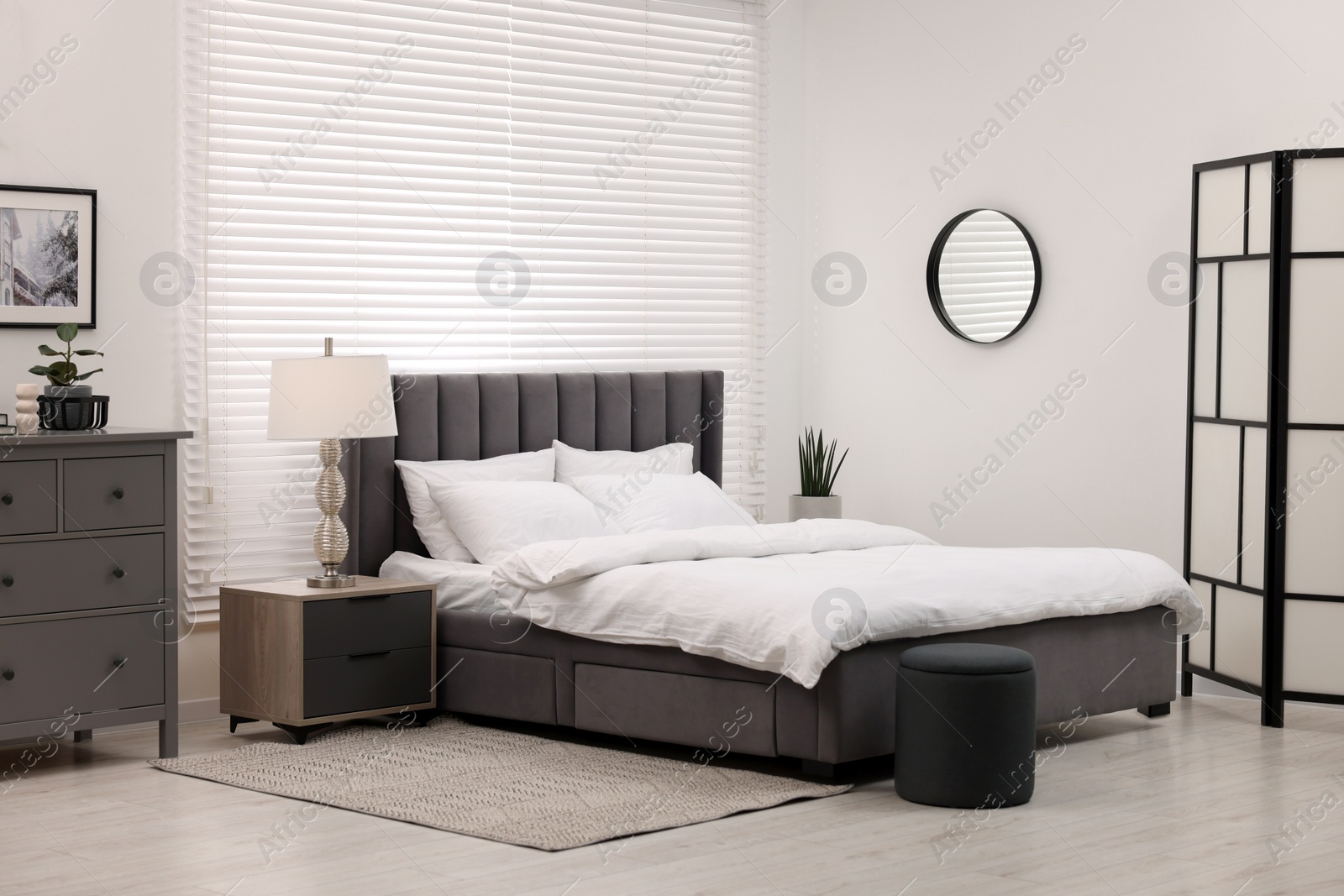 Photo of Stylish bedroom interior with large bed, chest of drawers and lamp