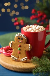 Tasty gingerbread man cookie and cocoa with marshmallows on blue wooden table