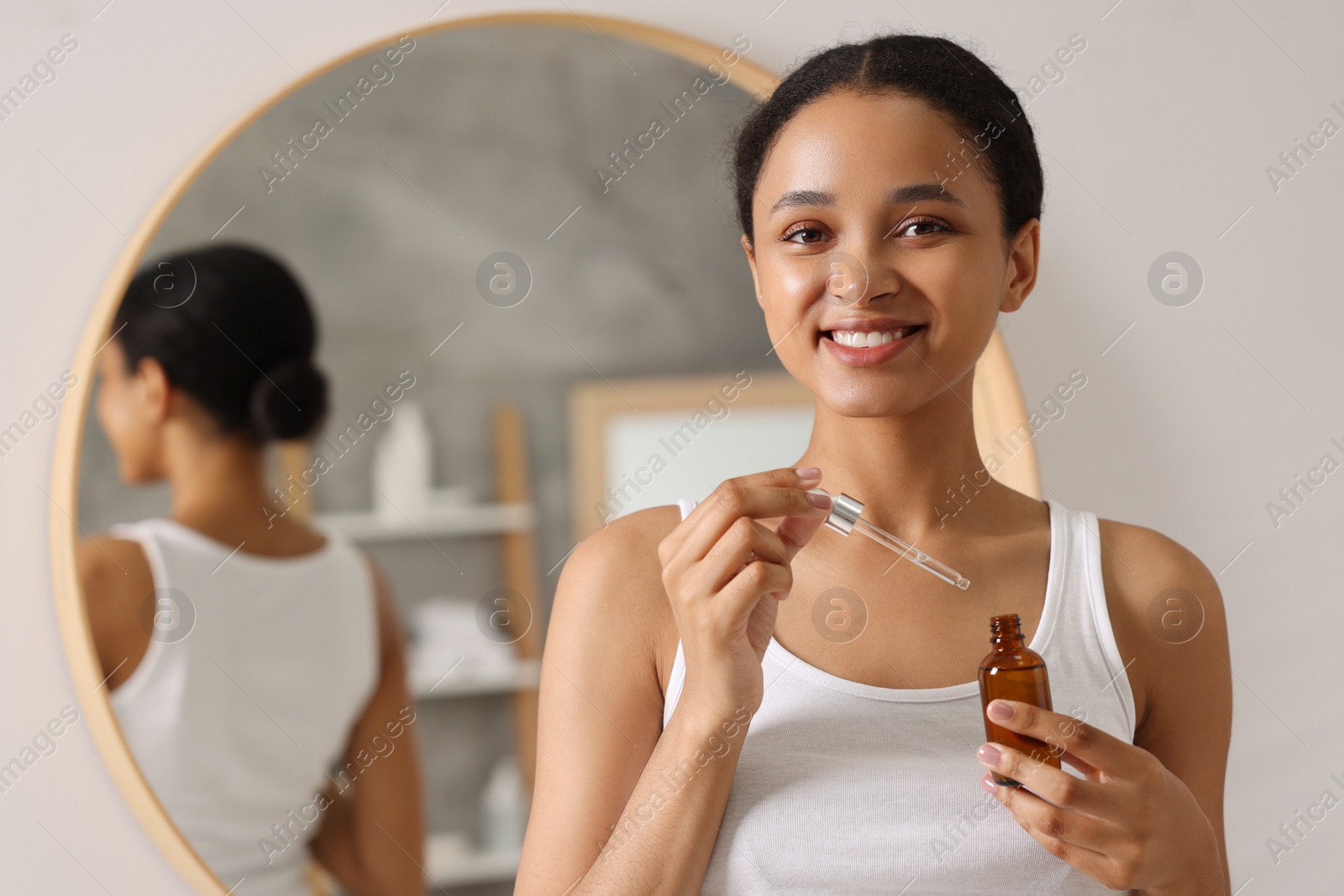 Photo of Smiling woman with bottle of serum and dropper in bathroom. Space for text