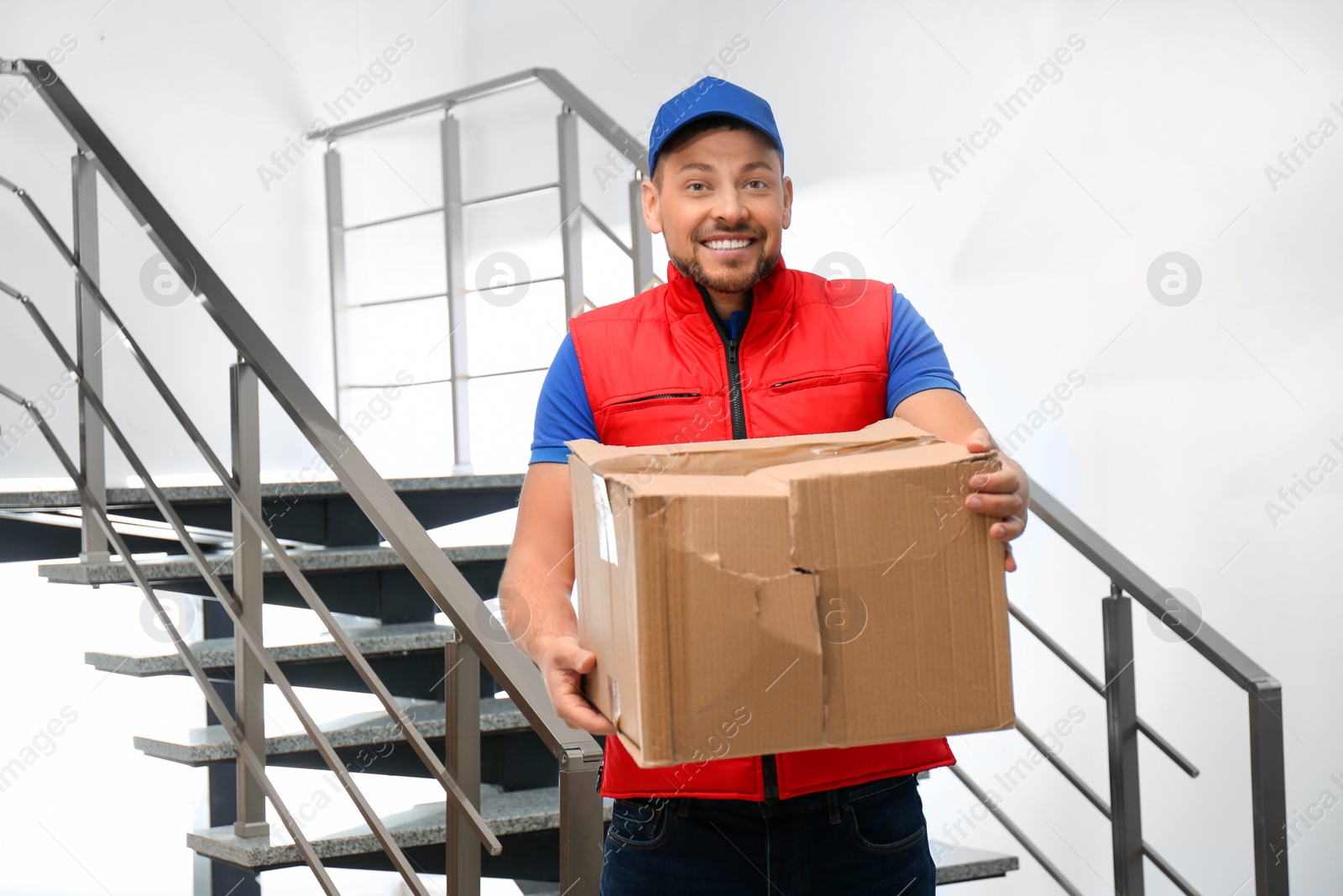 Photo of Emotional courier with damaged cardboard box indoors. Poor quality delivery service