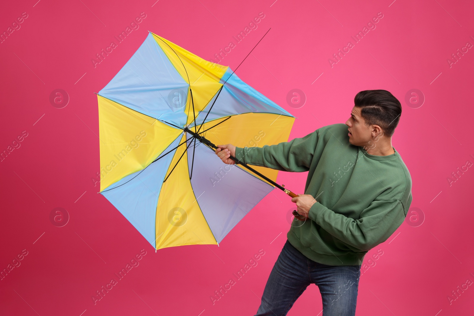 Photo of Man with umbrella caught in gust of wind on pink background