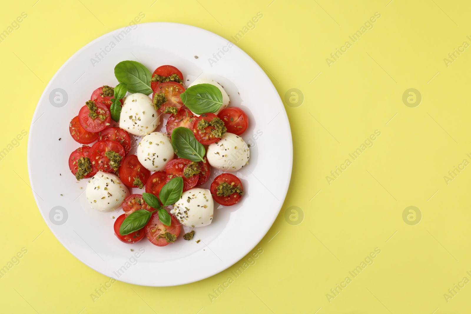 Photo of Tasty salad Caprese with tomatoes, mozzarella balls and basil on yellow background, top view. Space for text