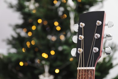 Guitar with cute Santa hat near Christmas tree, closeup. Space for text