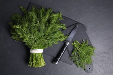 Sprigs of fresh green dill and knife on black table, top view