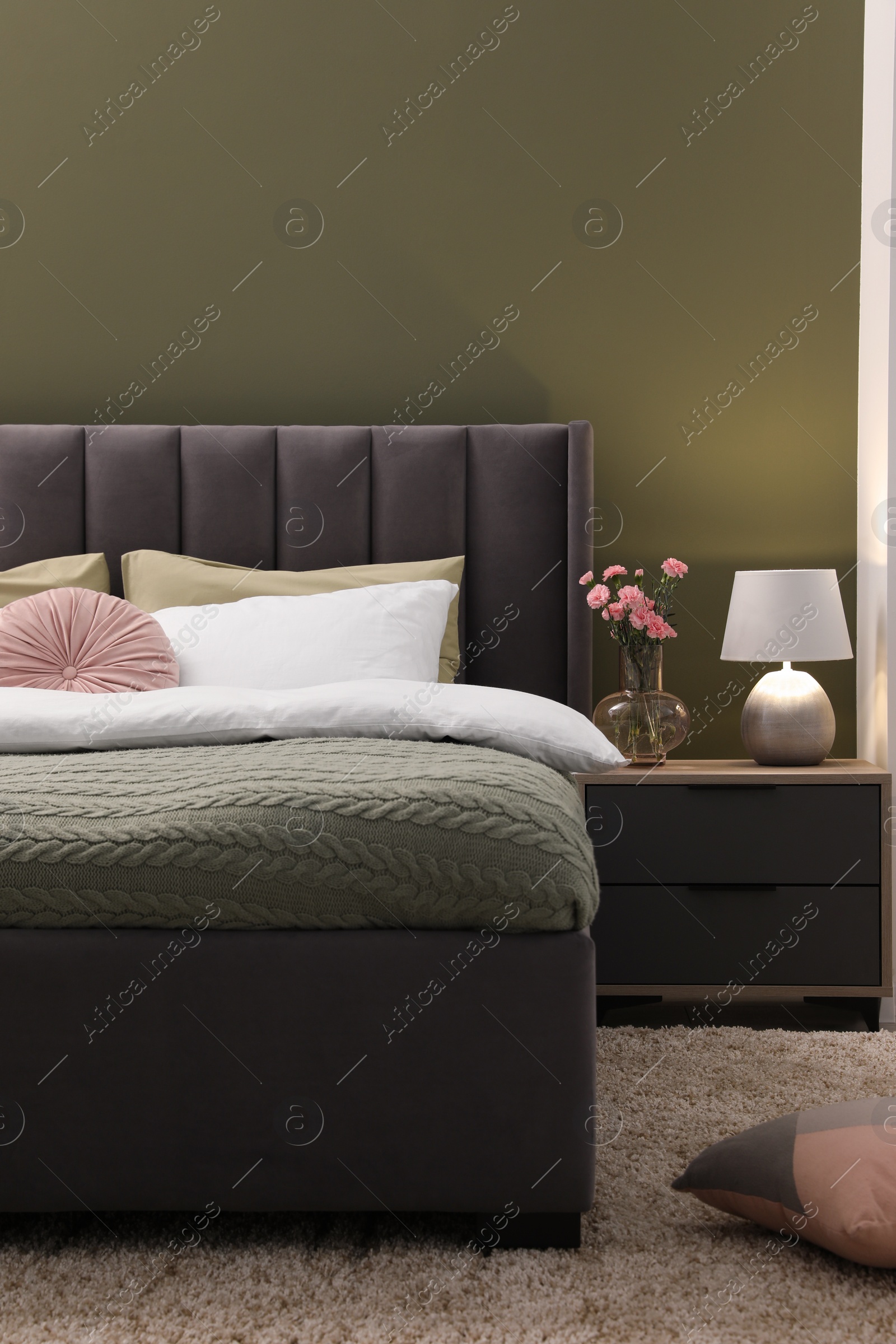 Photo of Large comfortable bed, nightstand, lamp and beautiful flowers in stylish room. Interior design