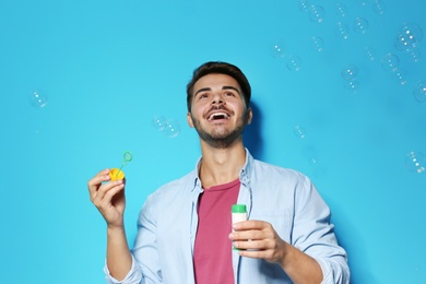 Young man blowing soap bubbles on color background