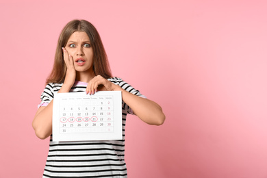 Emotional young woman holding calendar with marked menstrual cycle days on pink background. Space for text