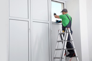 Worker on folding ladder installing window indoors