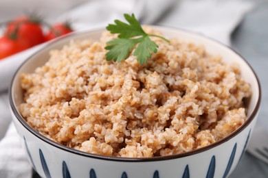 Photo of Tasty wheat porridge with parsley in bowl on table, closeup