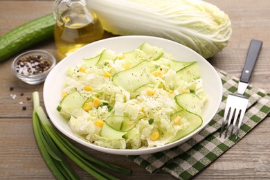 Photo of Tasty salad with Chinese cabbage in bowl and ingredients on wooden table, closeup