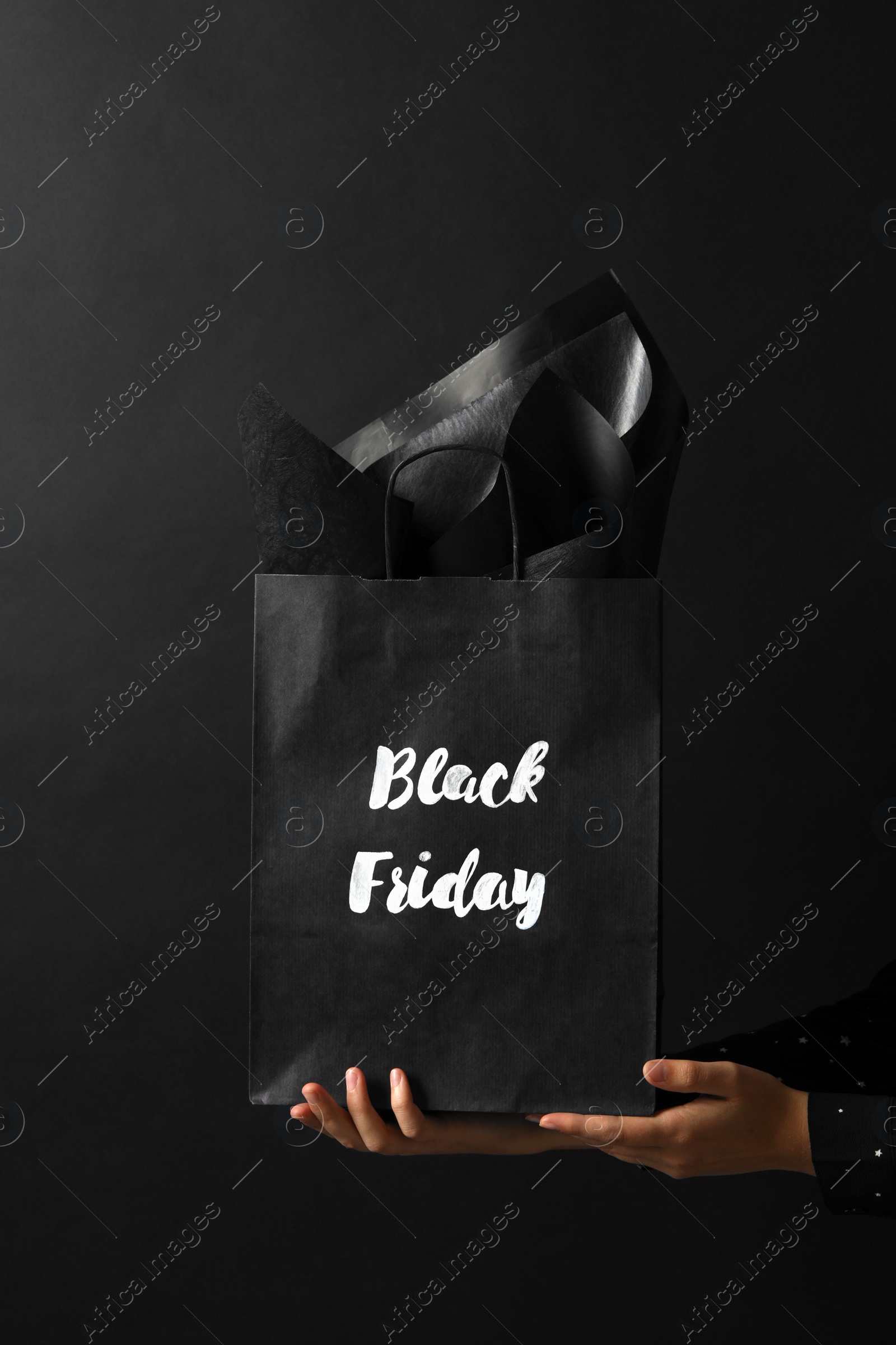 Photo of Woman holding shopping bag with words Black Friday on dark background, closeup