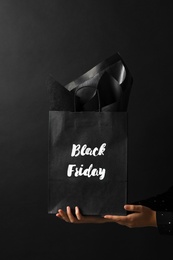 Woman holding shopping bag with words Black Friday on dark background, closeup