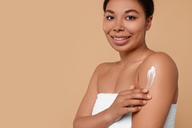 Young woman applying body cream onto shoulder on beige background, closeup. Space for text