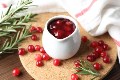 Photo of Cranberry sauce, fresh berries and rosemary on wooden table, closeup