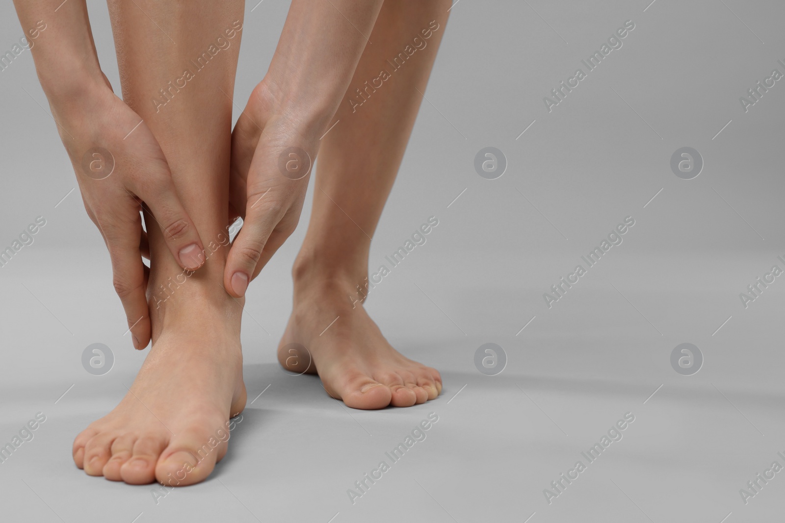 Photo of Woman suffering from leg pain on grey background, closeup. Space for text