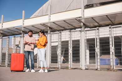 Photo of Being late. Worried couple with red suitcase outdoors, space for text