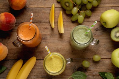 Photo of Mason jars of different tasty smoothies and fresh ingredients on wooden table, flat lay