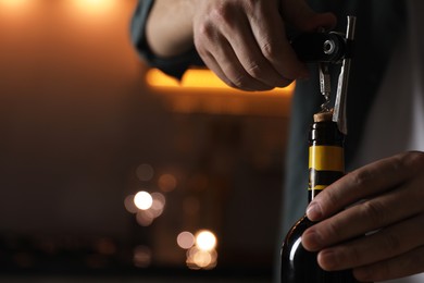 Man opening wine bottle with corkscrew on blurred background, closeup. Space for text