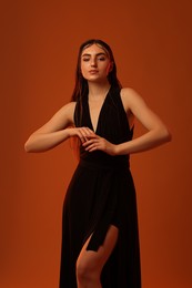 Beautiful woman in black dress posing on brown background