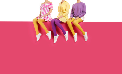 Group of women wearing bright tights and stylish shoes sitting on color background, closeup