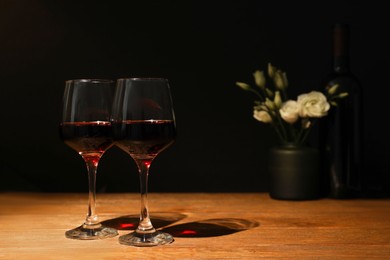 Glasses of wine and flowers on wooden table near dark wall