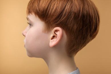 Photo of Hearing problem. Little boy on pale brown background, closeup