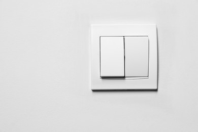 Modern plastic light switch on white wall, space for text