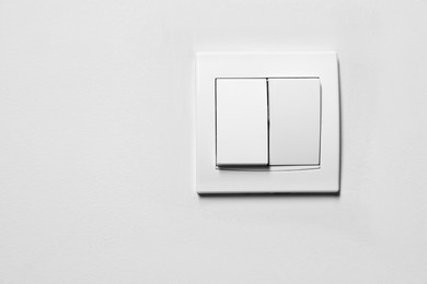 Photo of Modern plastic light switch on white wall, space for text