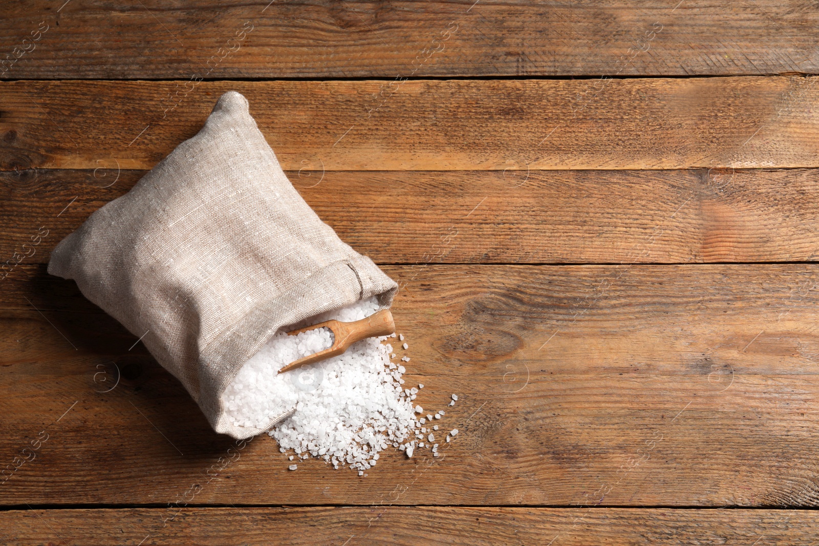 Photo of Bag of natural sea salt and scoop on wooden table, top view. Space for text