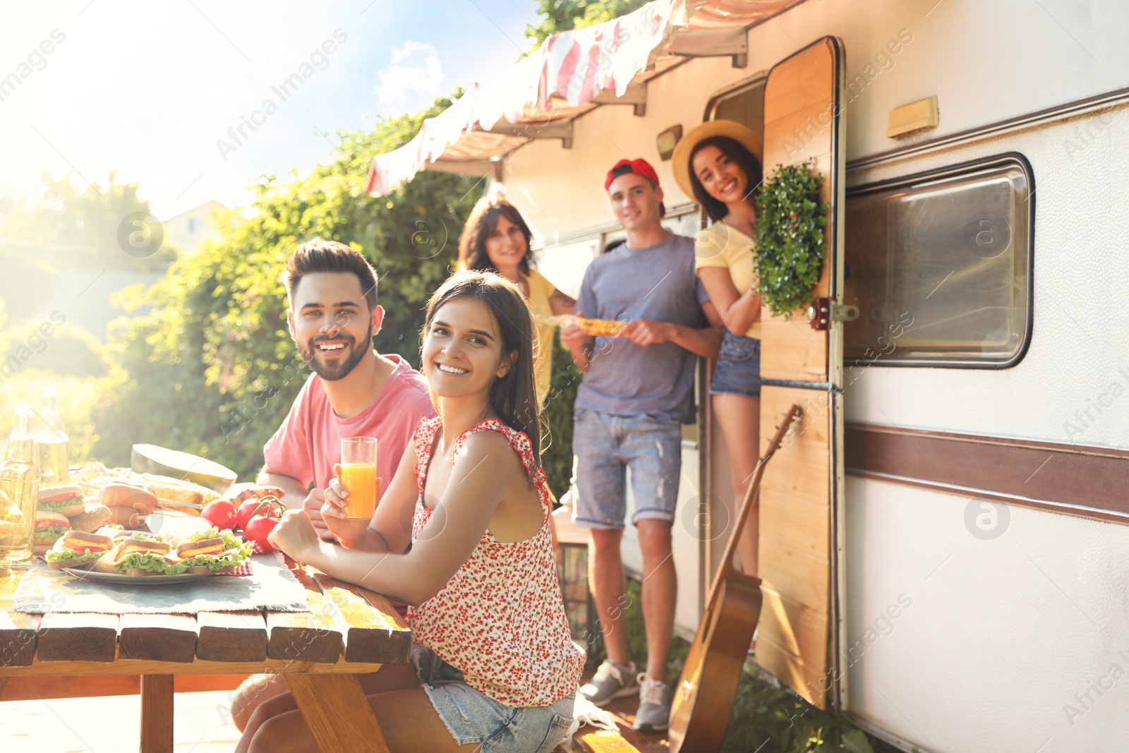 Photo of Happy friends with drinks and food near motorhome. Camping season