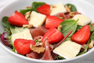 Photo of Tasty salad with brie cheese, prosciutto, strawberries and walnuts in bowl, closeup