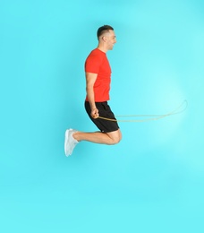 Young sportive man training with jump rope on color background