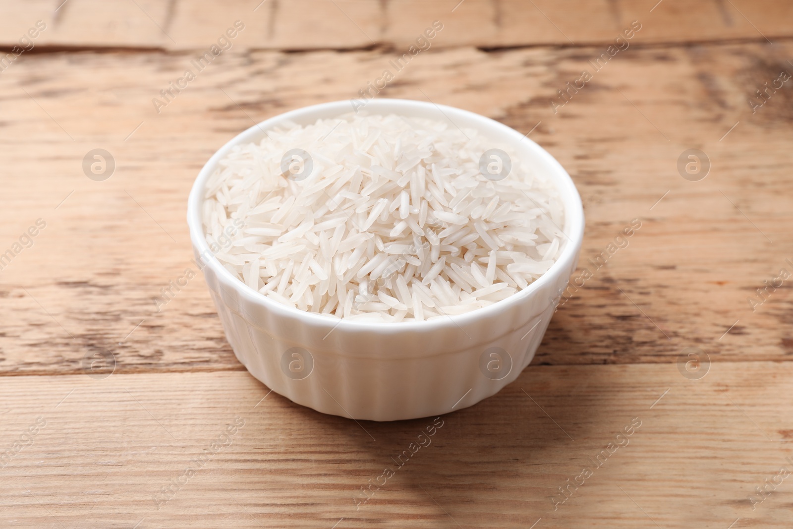 Photo of Raw basmati rice in bowl on wooden table