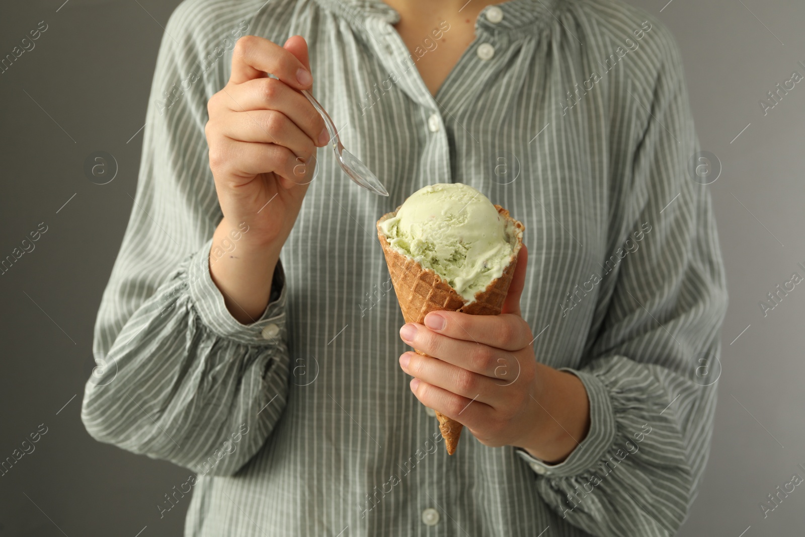 Photo of Woman eating green ice cream in wafer cone on grey background, closeup