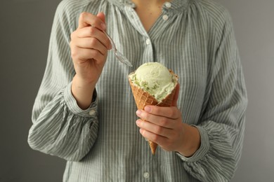 Photo of Woman eating green ice cream in wafer cone on grey background, closeup