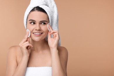 Young woman cleaning her face with cotton pads on beige background. Space for text