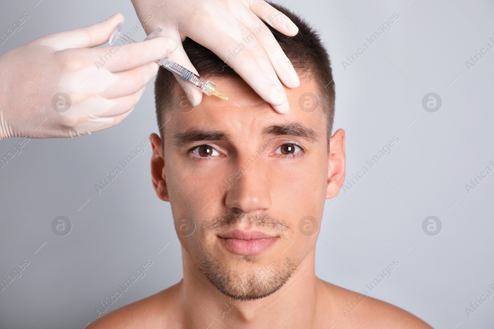 Photo of Man getting facial injection on grey background, closeup. Cosmetic surgery