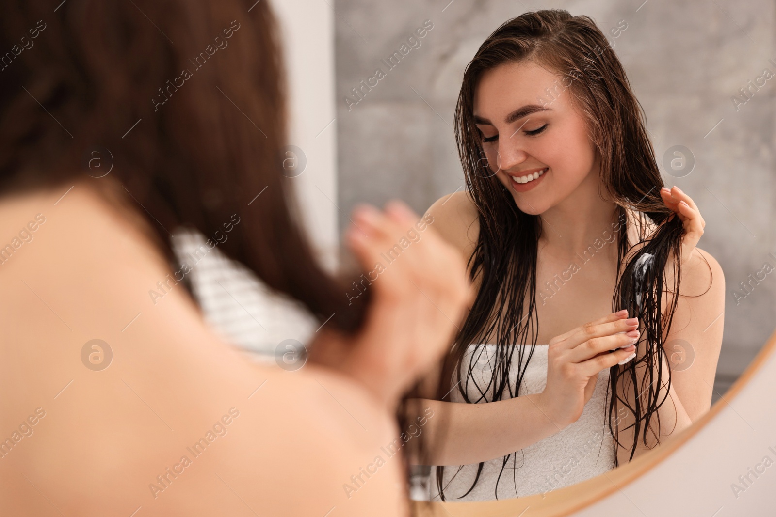 Photo of Young woman applying hair mask near mirror in bathroom